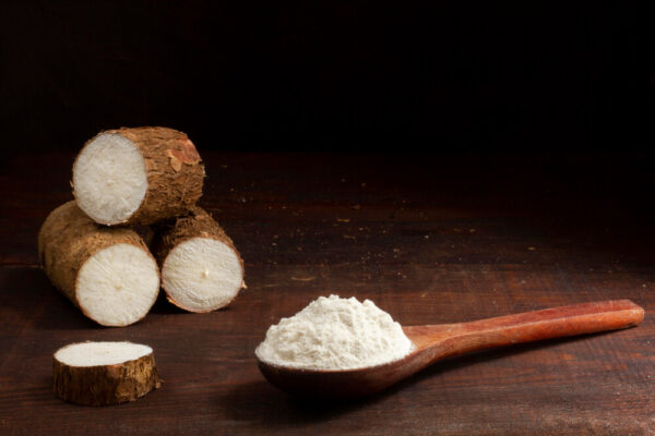 Cassava roots and flour on wooden spoon.
