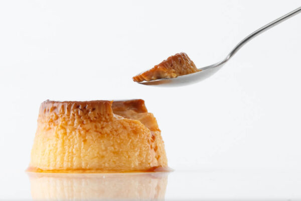 Flan dessert with spoon on white background.