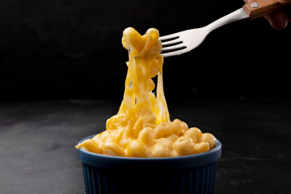 Cheesy macaroni being lifted by fork.