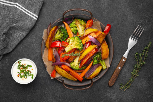 Roasted vegetables with dip on dark background.