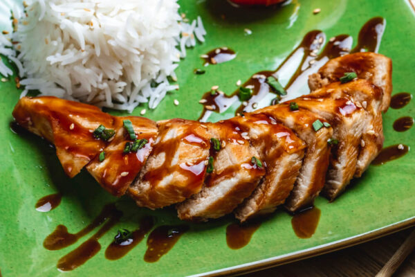 Sliced teriyaki chicken with rice on plate.